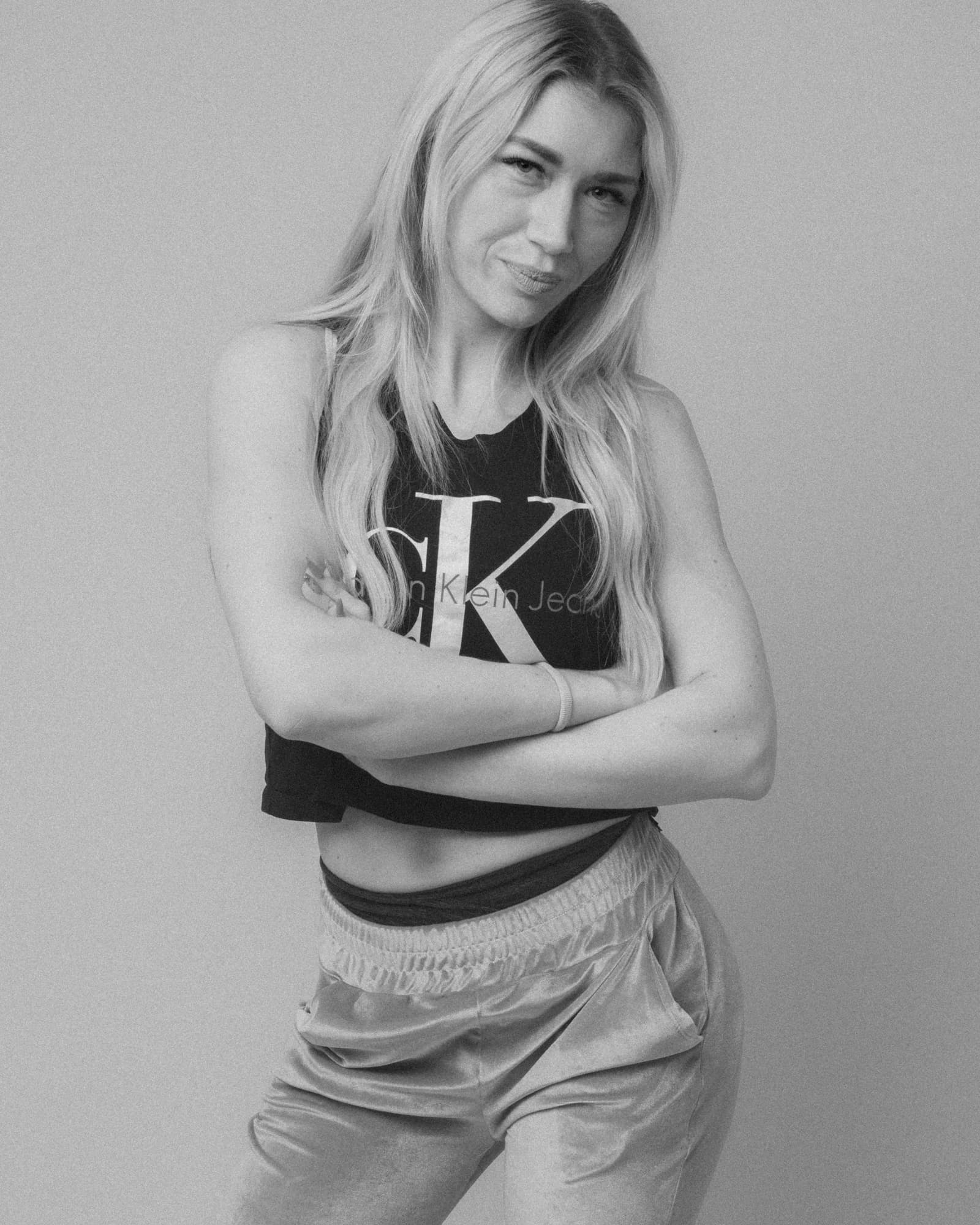 Black and white portrait of a blonde woman standing with crossed arms.