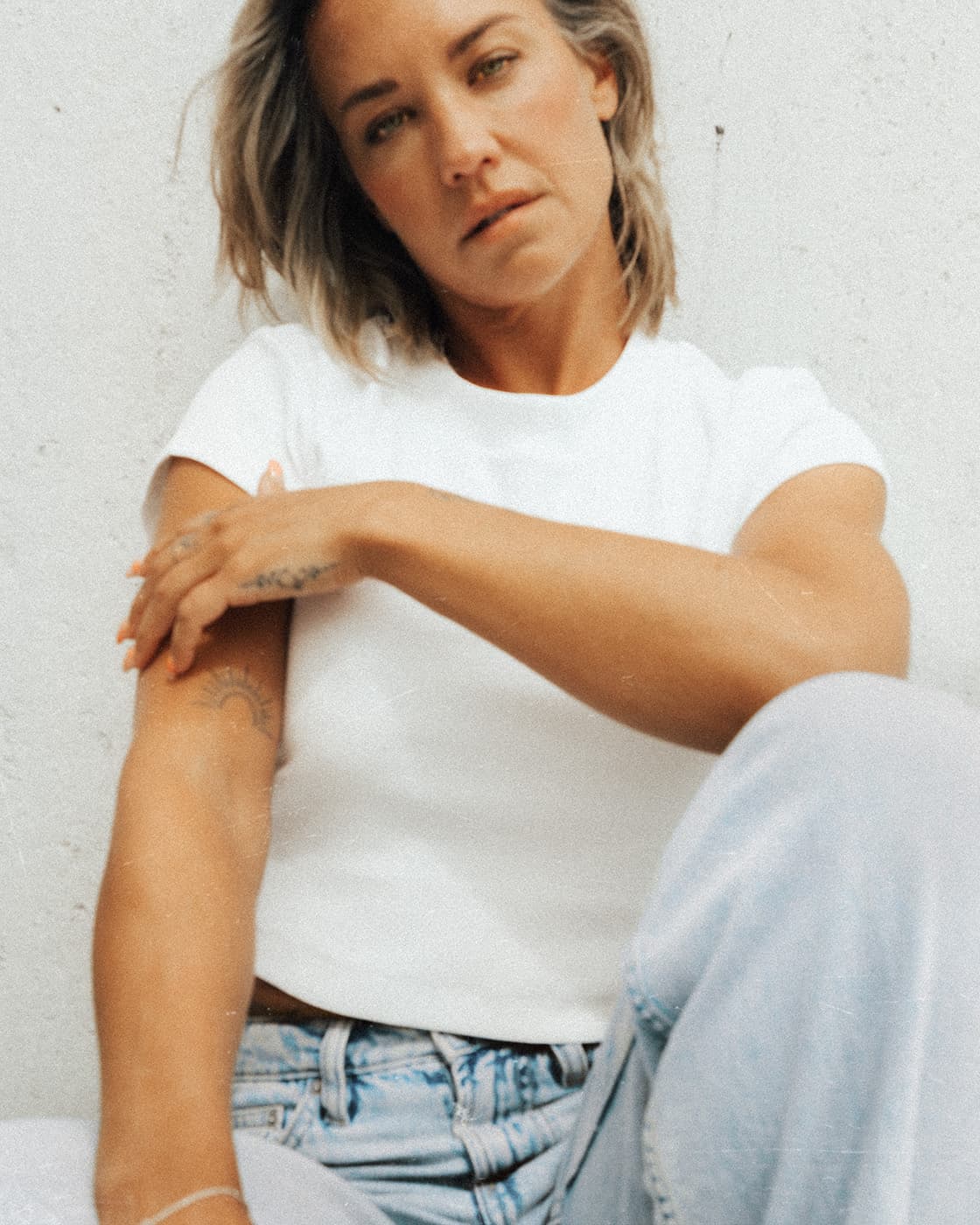 Color portrait of a woman in a white t-shirt and light jeans sitting against a pale wall.