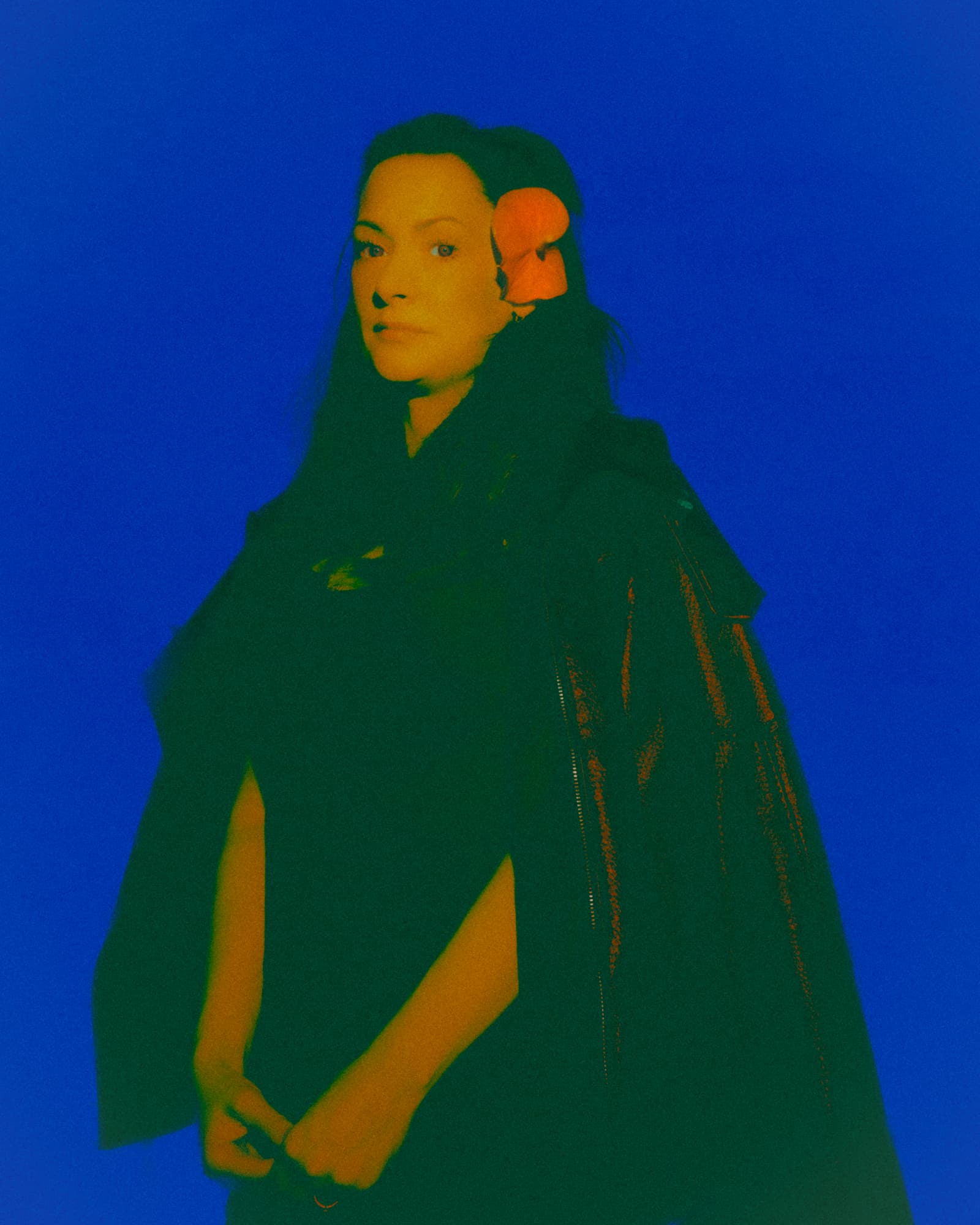 Color-shifted portrait of a woman with an orange flower in her hair against a vivid blue background.