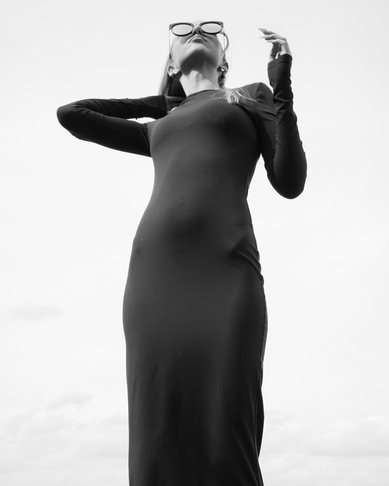 Black and white low-angle portrait of a woman in sunglasses and a long black dress.