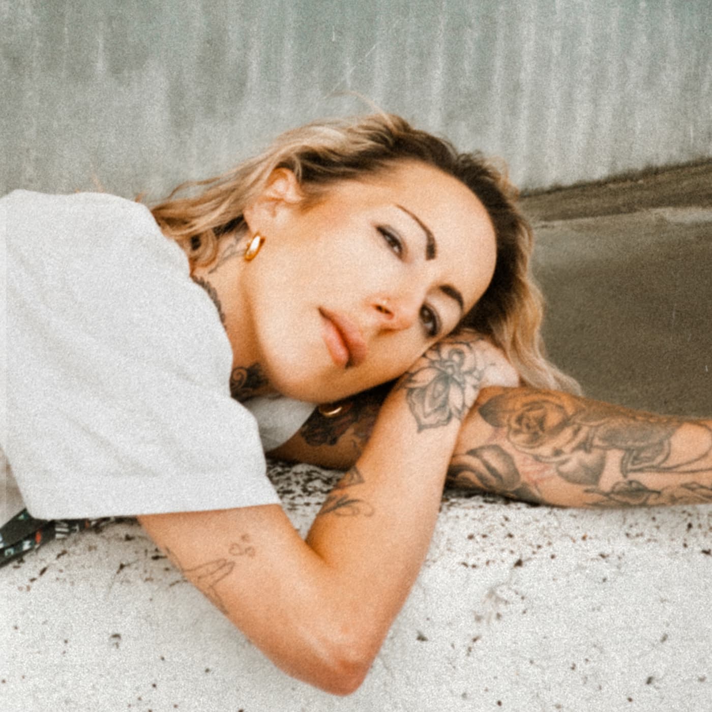 Color portrait of a tattooed woman lying sideways on a speckled floor.