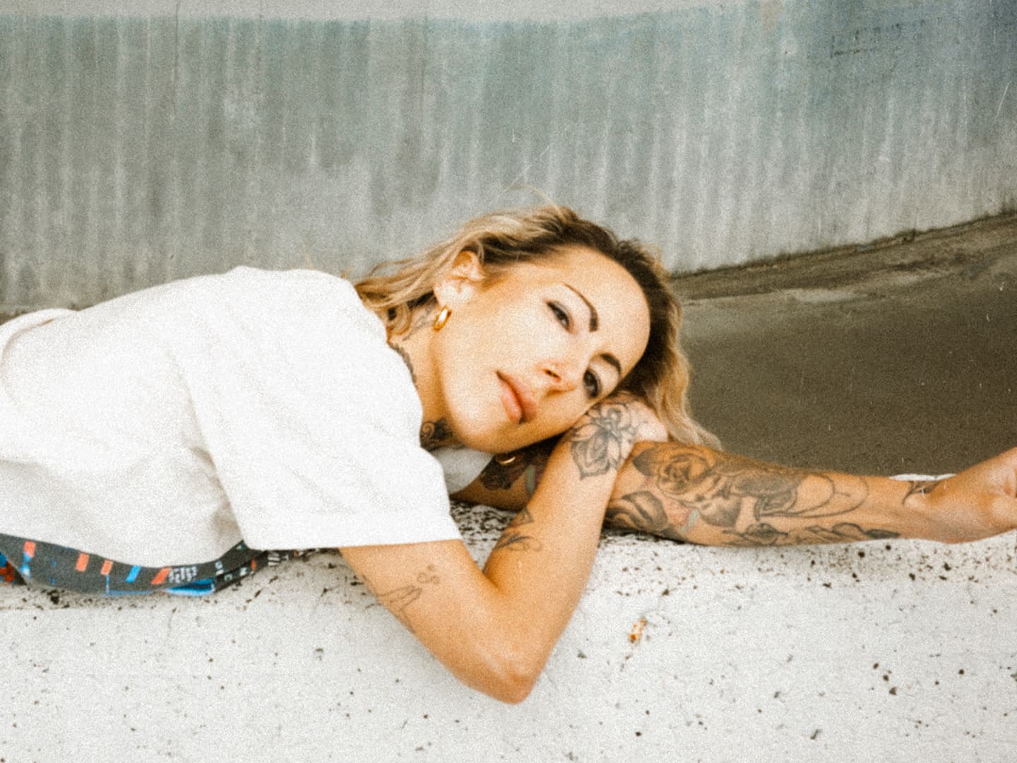 Color portrait of a tattooed woman lying sideways on a speckled floor.