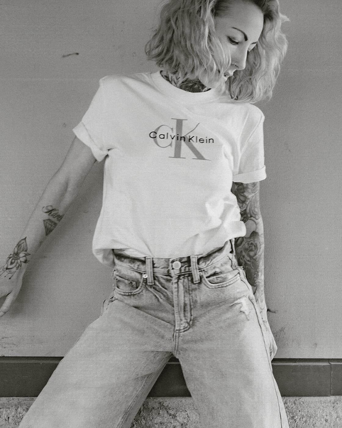 Black and white portrait of a tattooed woman in a white t-shirt and jeans.