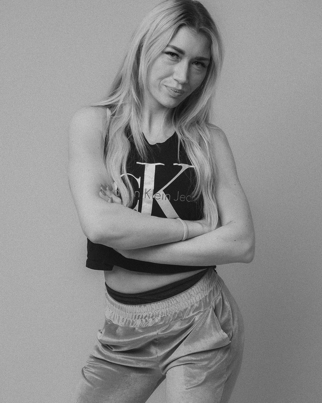 Black and white portrait of a blonde woman standing with crossed arms.