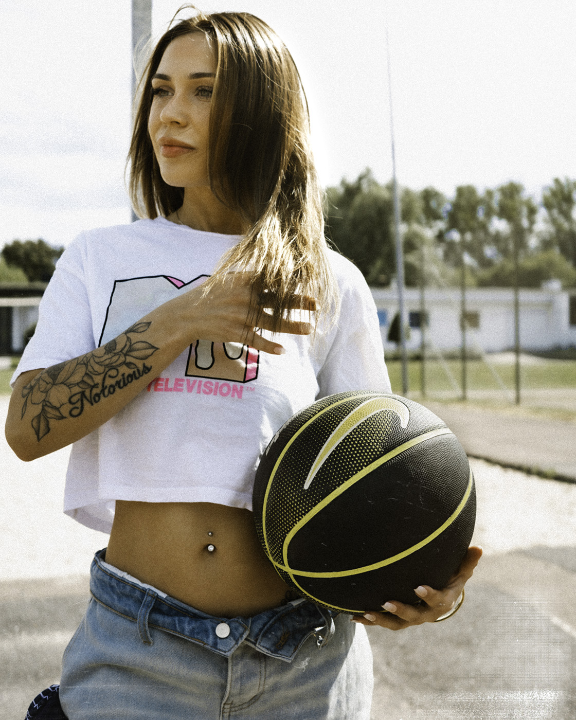 Color portrait of a woman in a white MTV t-shirt holding a black basketball outdoors.