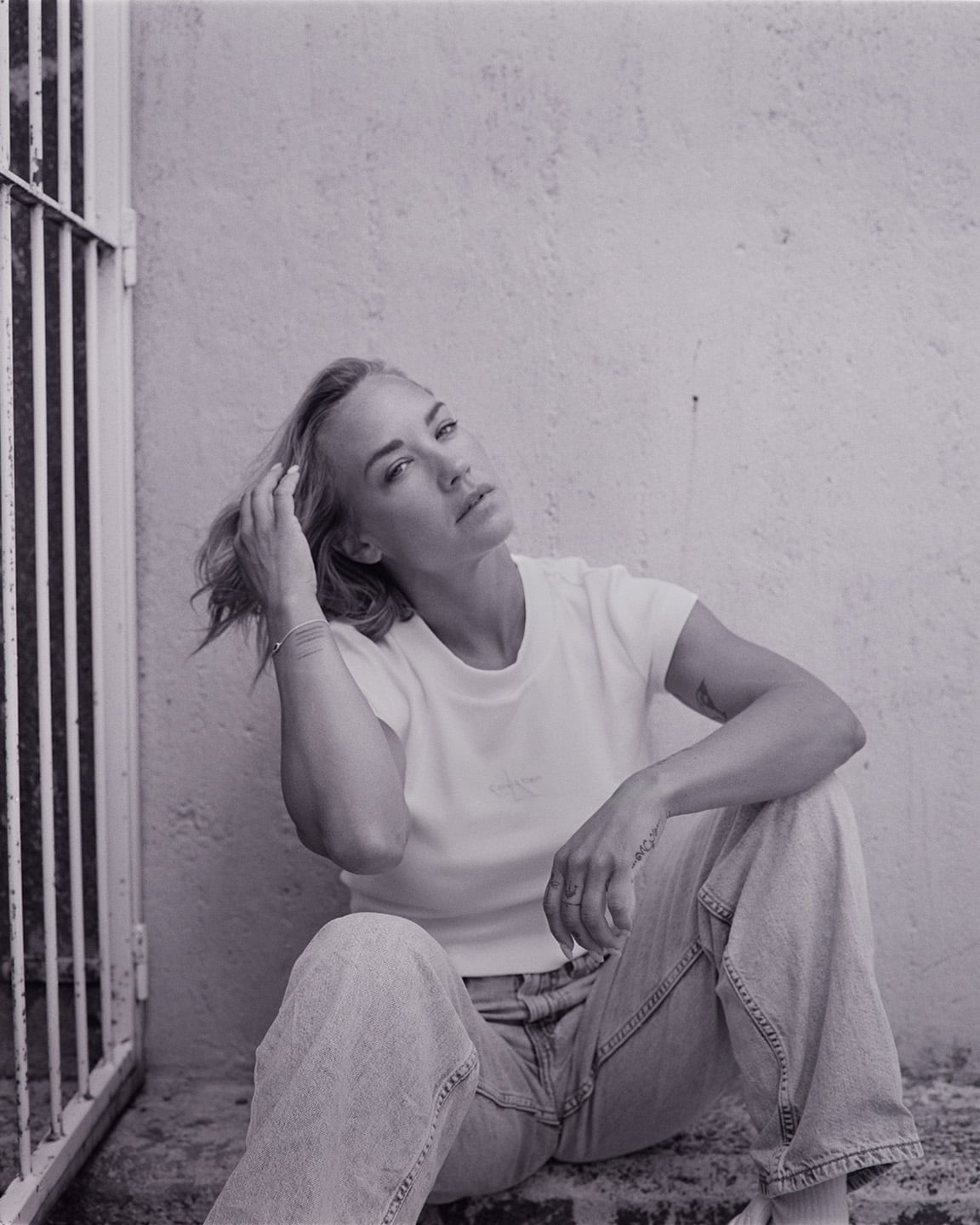 Black and white portrait of a blonde woman sitting against a textured wall.