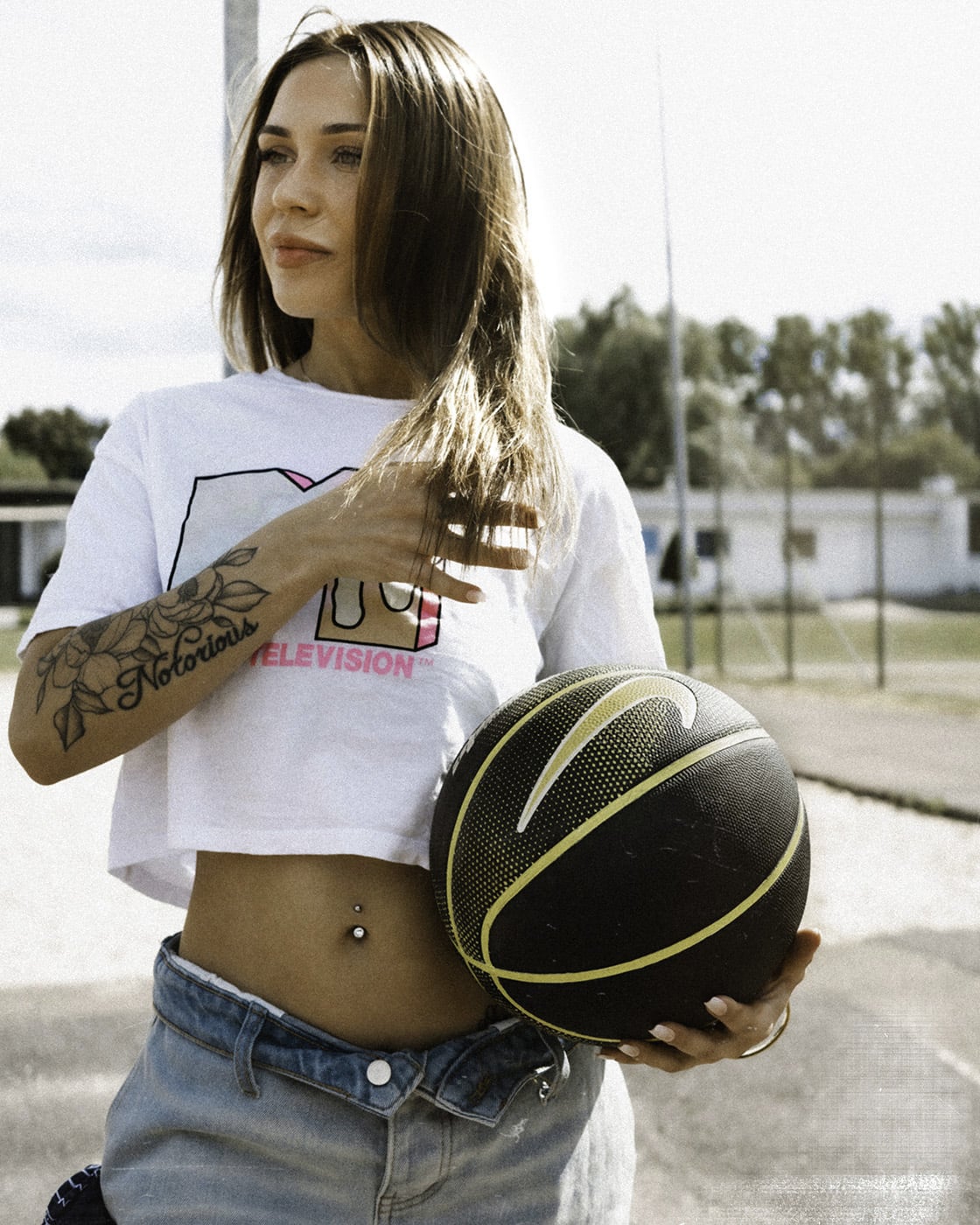 Color portrait of a woman in a white MTV t-shirt holding a black basketball outdoors.